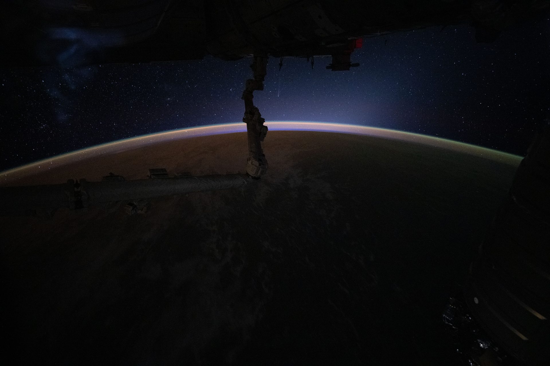 La cometa C/2025 R3 (PANSTARRS) e la sua debole coda sopra l'orizzonte luminoso della Terra, fotografate dalla Stazione Spaziale Internazionale