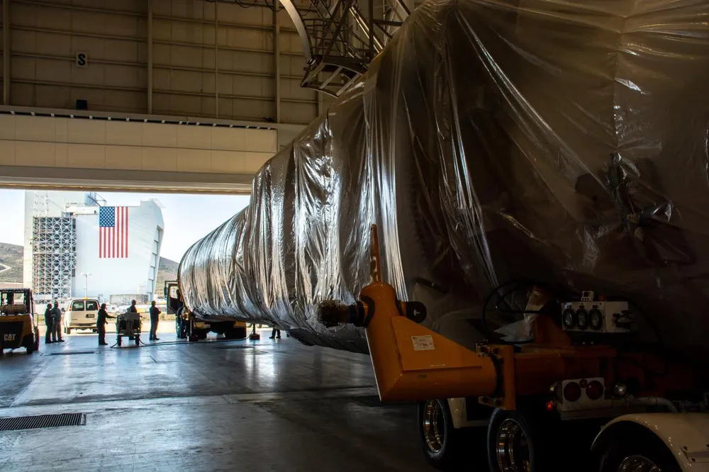 Un lungo booster razzo bianco su un trasportatore che lascia un hangar